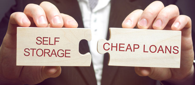 A person holds two puzzle pieces that fit together. One puzzle piece says "self-storage" and the other says "cheap loans".